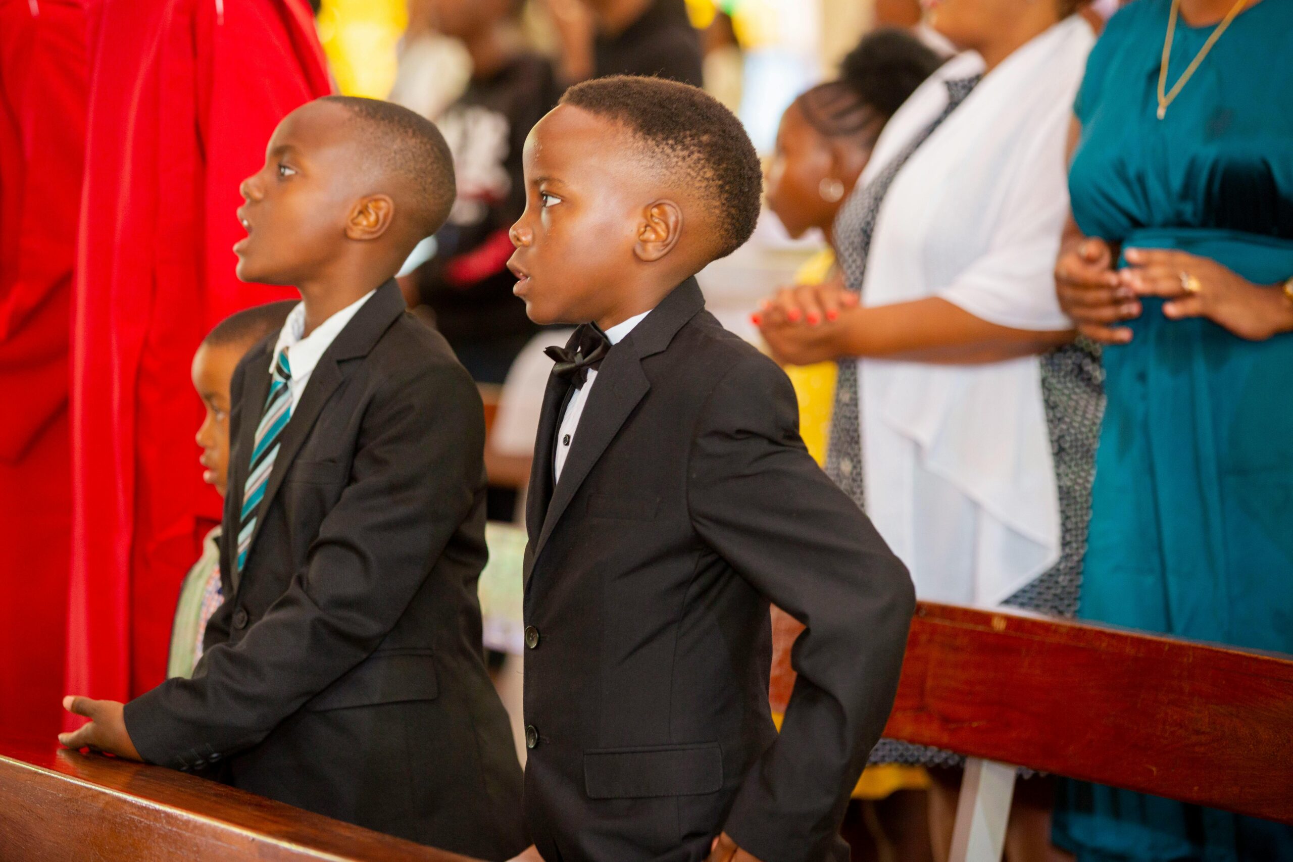 Two young boys in formal suits attentively participate in a church ceremony.